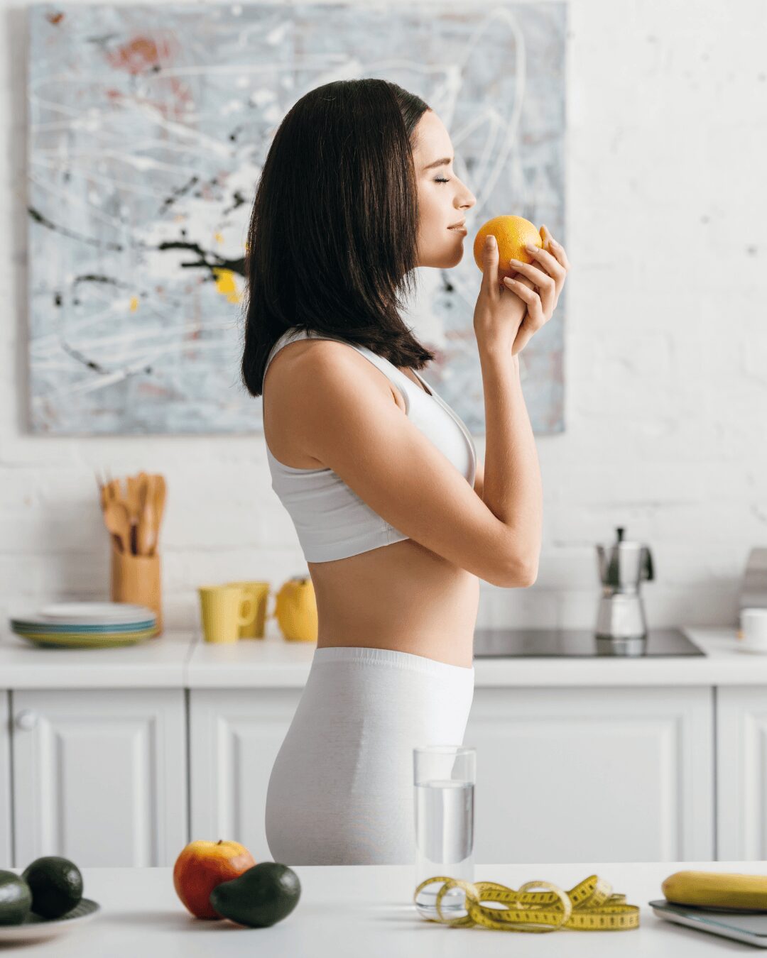 Chica oliendo una fruta en la cocina.