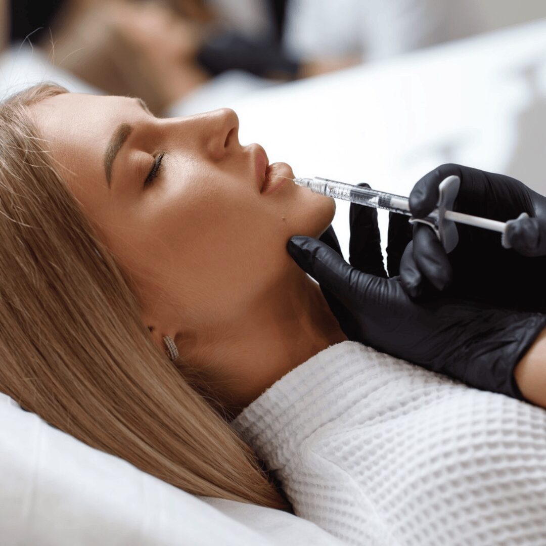 Unas manos pinchando una cara de una chica joven estirada en una camilla